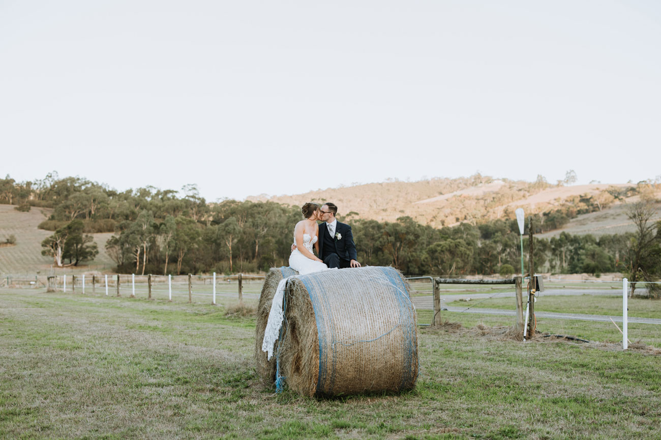 bride and groom sitting on a large hay bale with a stunning yarra valley backdrop
